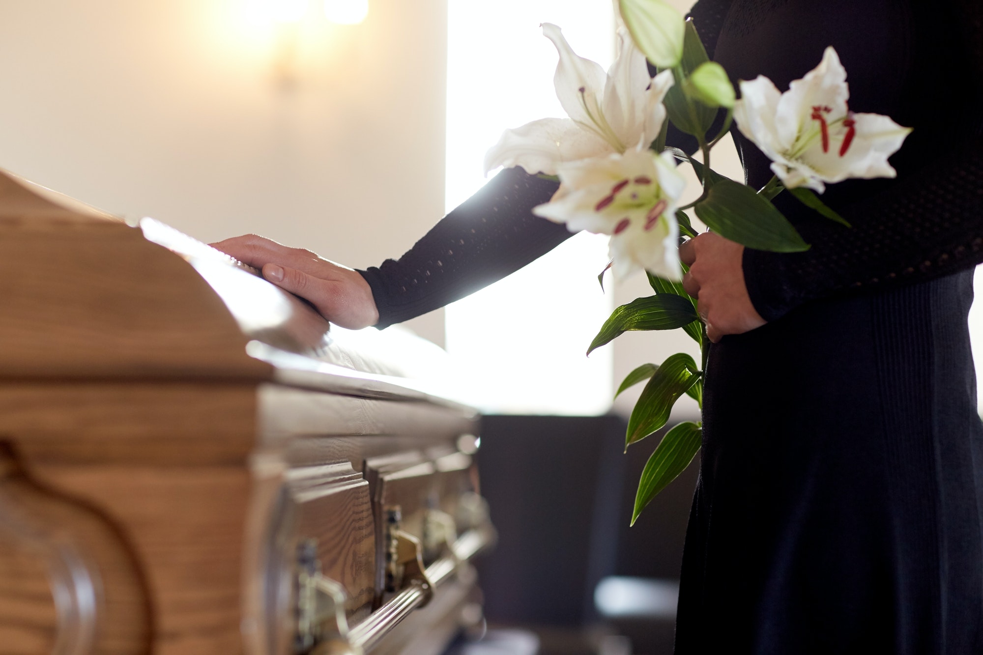 woman-with-lily-flowers-and-coffin-at-funeral.jpg