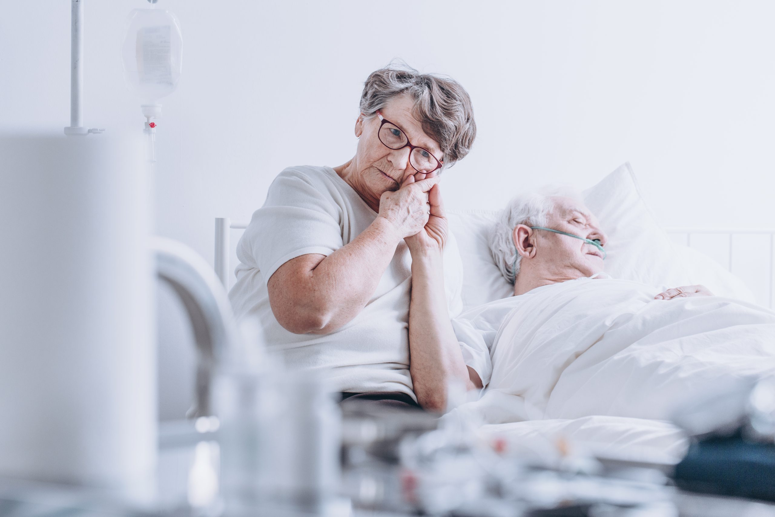 Loving wife sitting at her husband's hospital bed and holding his hand